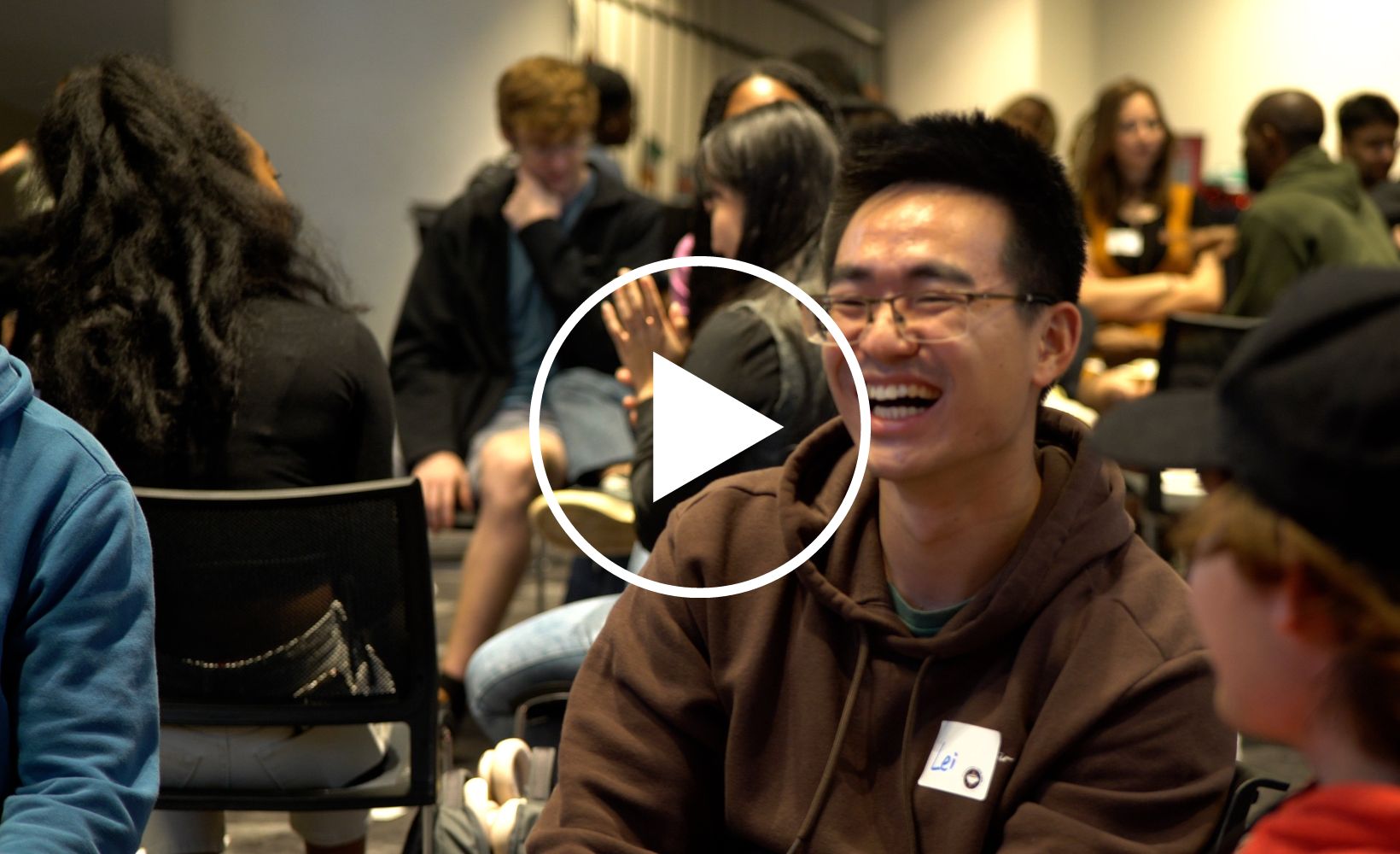 Lei Jin sitting in the Victor K Wilson Memorial Hall Ballroom surrounded by other students all laughing at International Coffee Hour